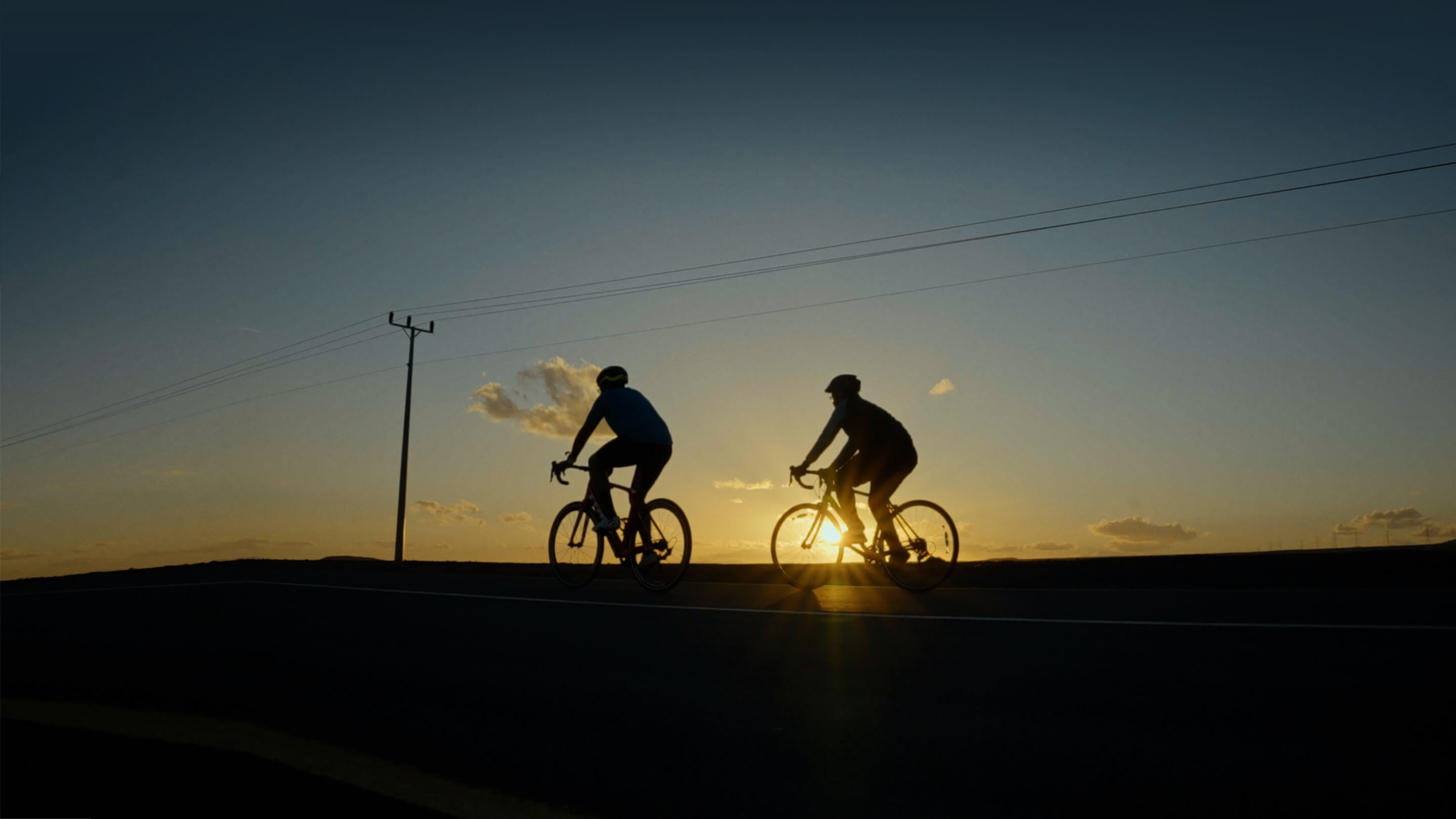 Silhouette Of The Two Cyclist Riding A Road Bike At Sunset 